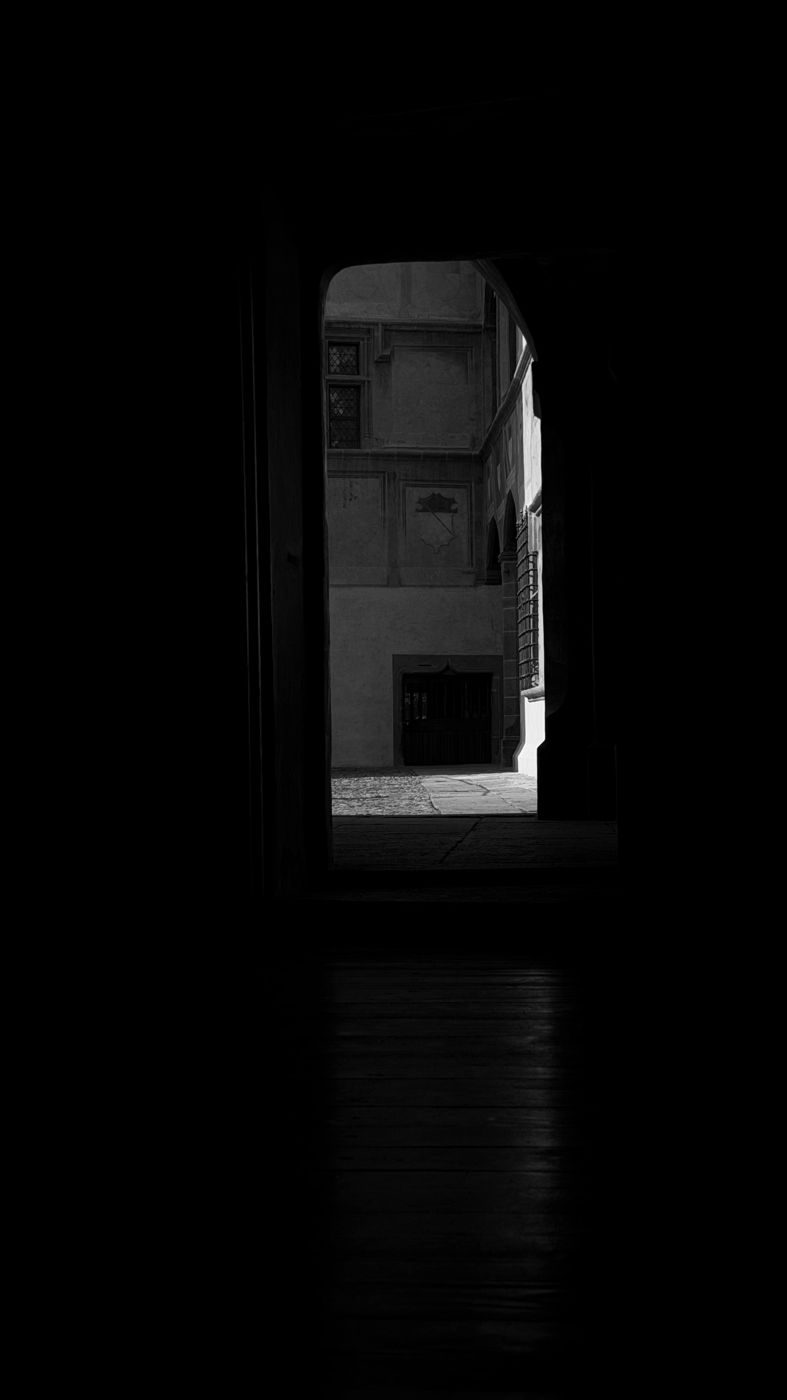 Dal buio di un corridoio del castello, una porta si apre sul cortile affrescato